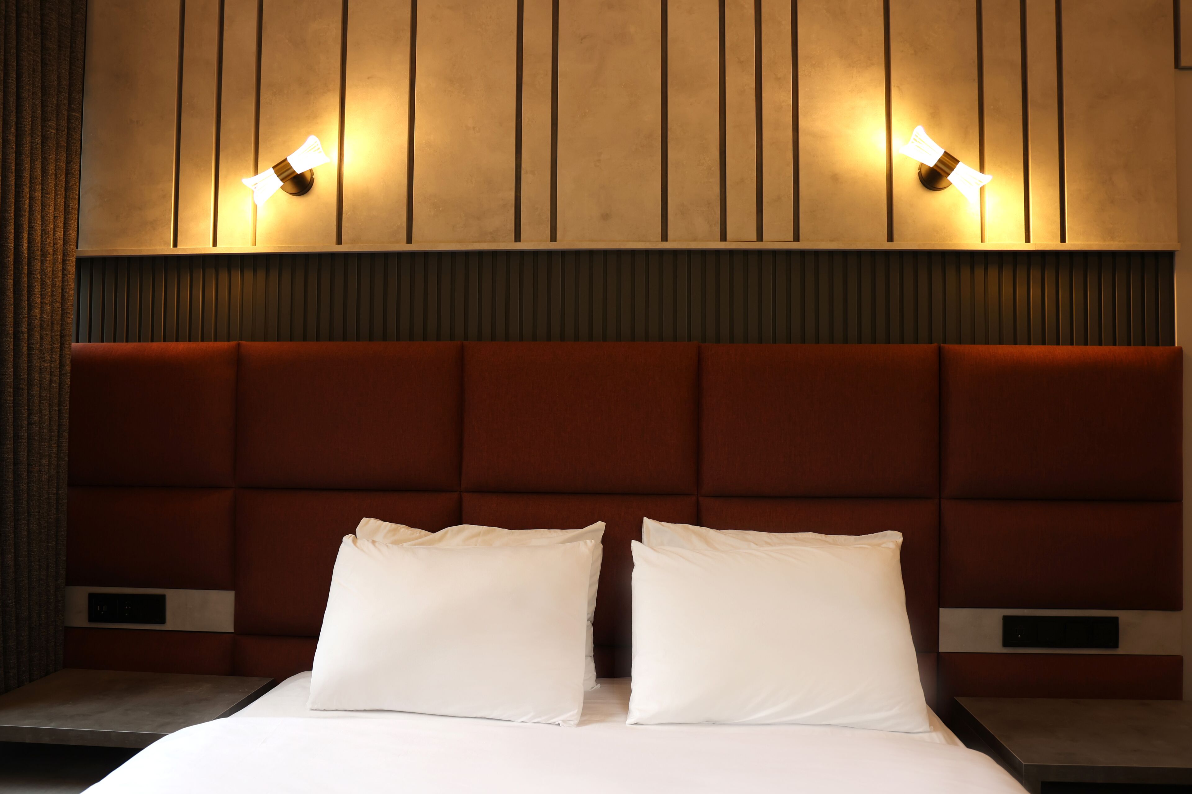 A hotel room with a large bed, two bedside tables, and a headboard with vertical lines.