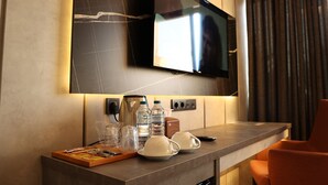 A hotel room with a flat-screen TV mounted on the wall, a coffee maker, water bottles, glasses, and a small table with a remote control. - Hotel Lazlakar (Çayeli)