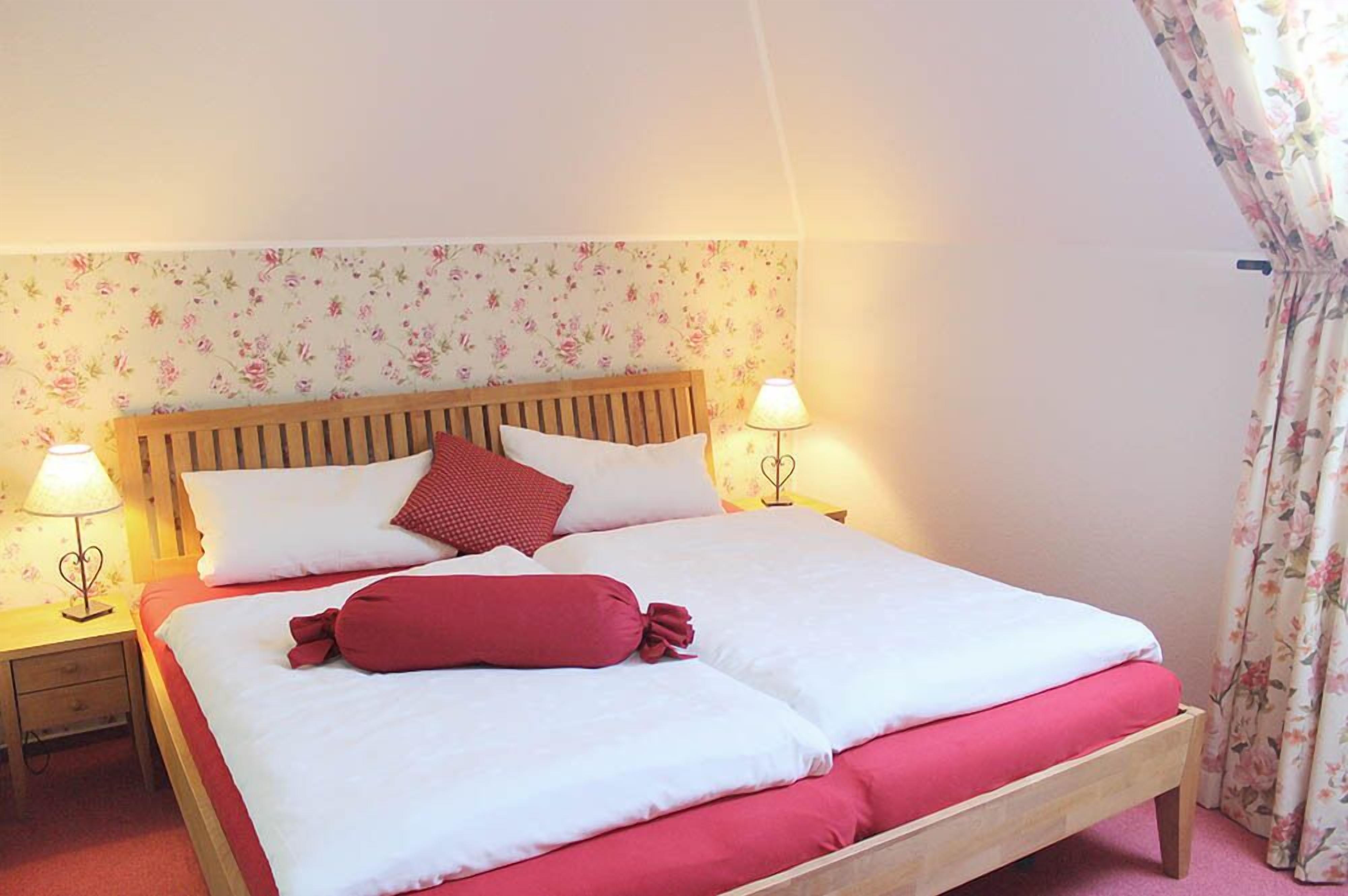 A neatly made bed with white and red bedding, two bedside lamps, and a floral-patterned headboard.