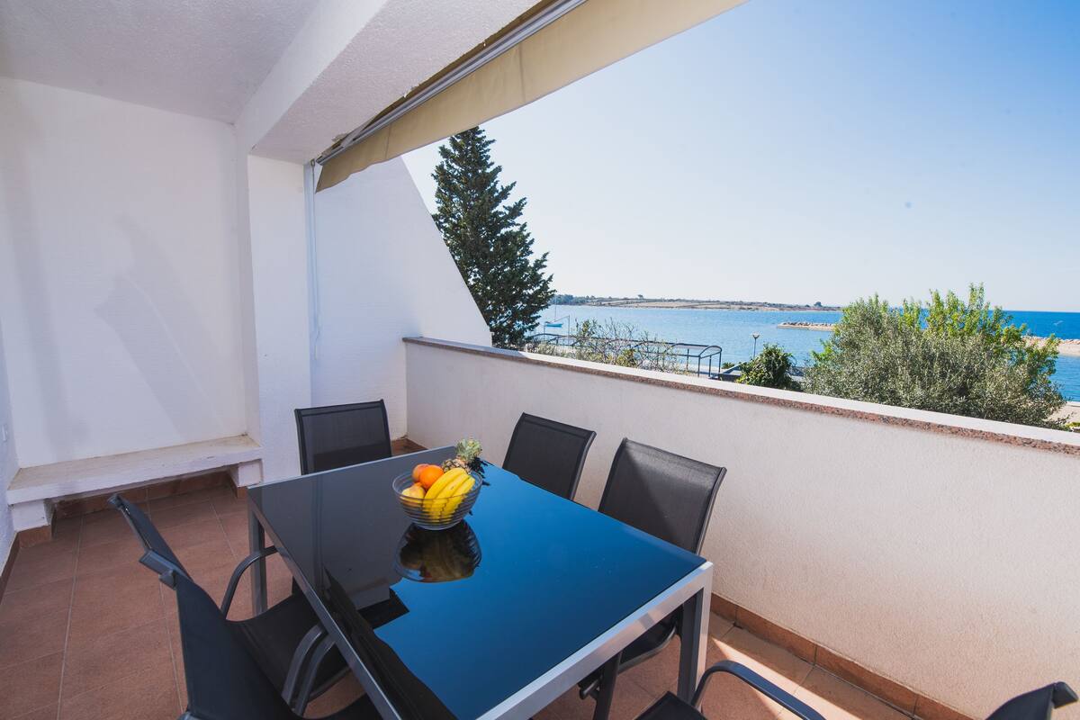 A balcony with a table, chairs, and a bowl of fruit.