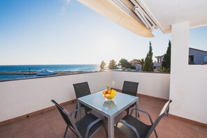 Un balcón con mesa y sillas, un frutero y vistas al mar y a los barcos.