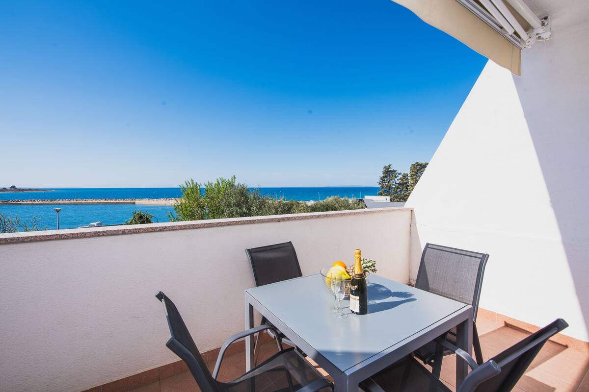 A balcony with a table set for two, overlooking a beach and the sea.