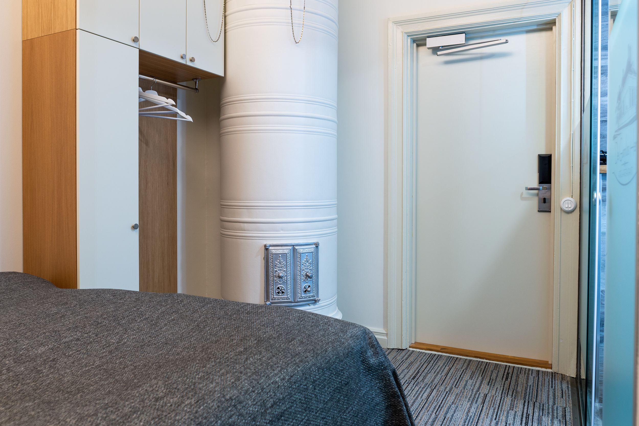 Une chambre d’hôtel avec un lit, une armoire, une colonne cylindrique et une porte.