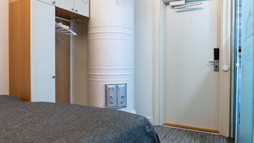 Une chambre d’hôtel avec un lit, une armoire, une colonne cylindrique et une porte.
