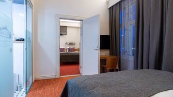 A hotel room with a bed, a desk, a chair, a TV, and a bathroom visible through an open door.