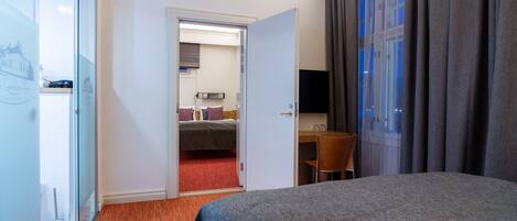 Habitación de hotel con cama, escritorio, silla, televisor y baño visible a través de una puerta abierta.