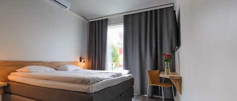 Una habitación de hotel moderna con una cama, mesita de noche, lámpara y un escritorio con silla.