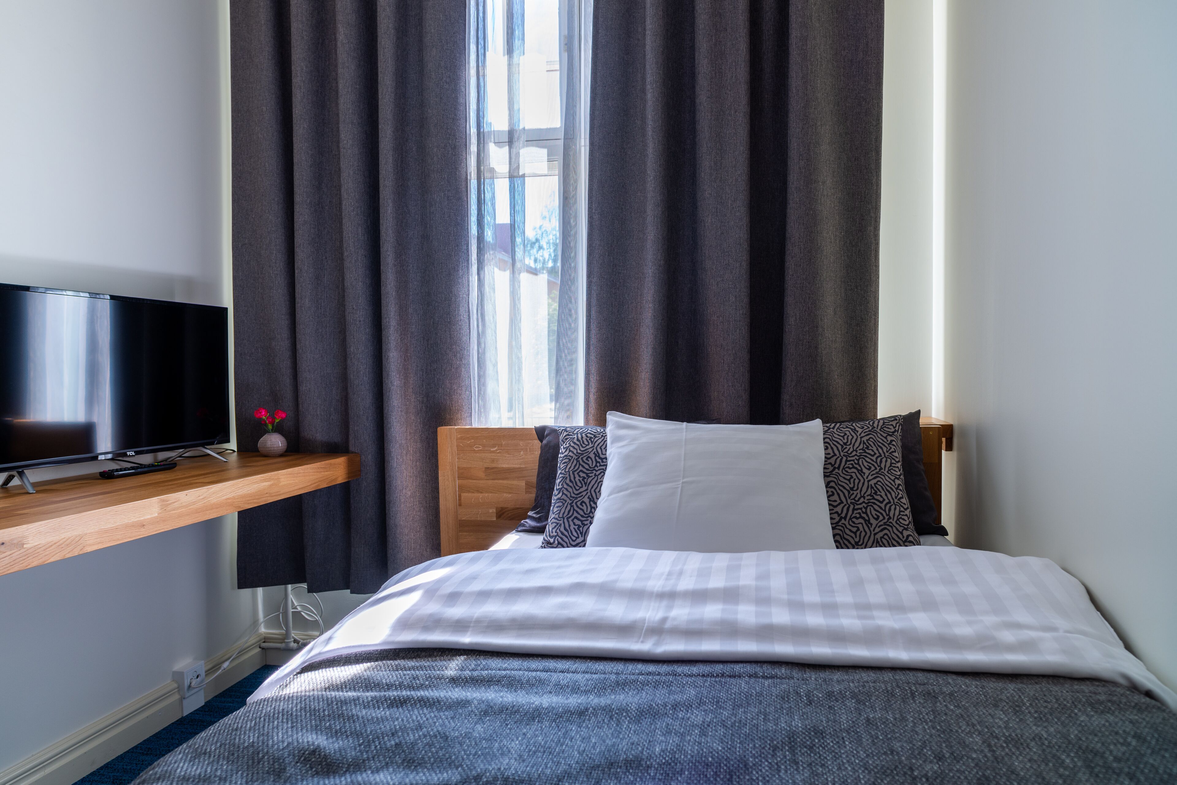 Una habitación de hotel con una cama, un televisor sobre una repisa de madera y una ventana con cortinas.