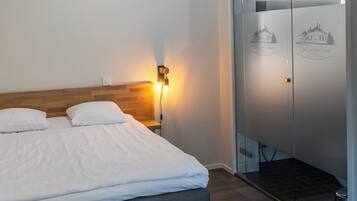 Une chambre d’hôtel moderne avec un grand lit, une table de chevet avec une lampe, une armoire à portes vitrées et une petite plante en pot accrochée au mur.