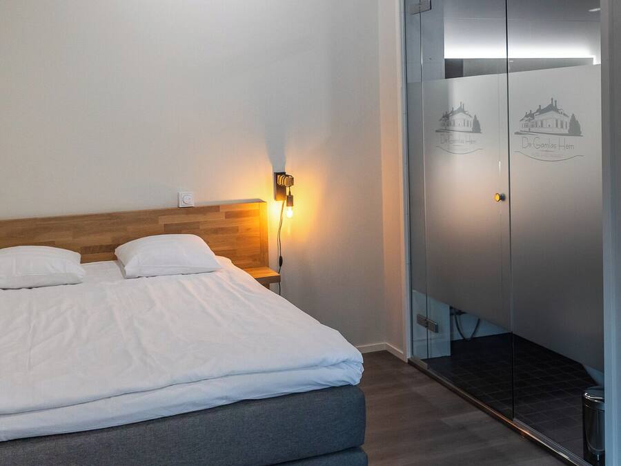 Une chambre d’hôtel moderne avec un grand lit, une table de chevet avec une lampe, une armoire à portes vitrées et une petite plante en pot accrochée au mur.