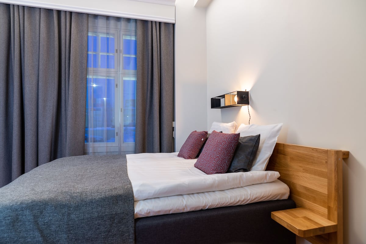 Una cama bien hecha con un edredón gris, un cabecero de madera y dos almohadas estampadas.
