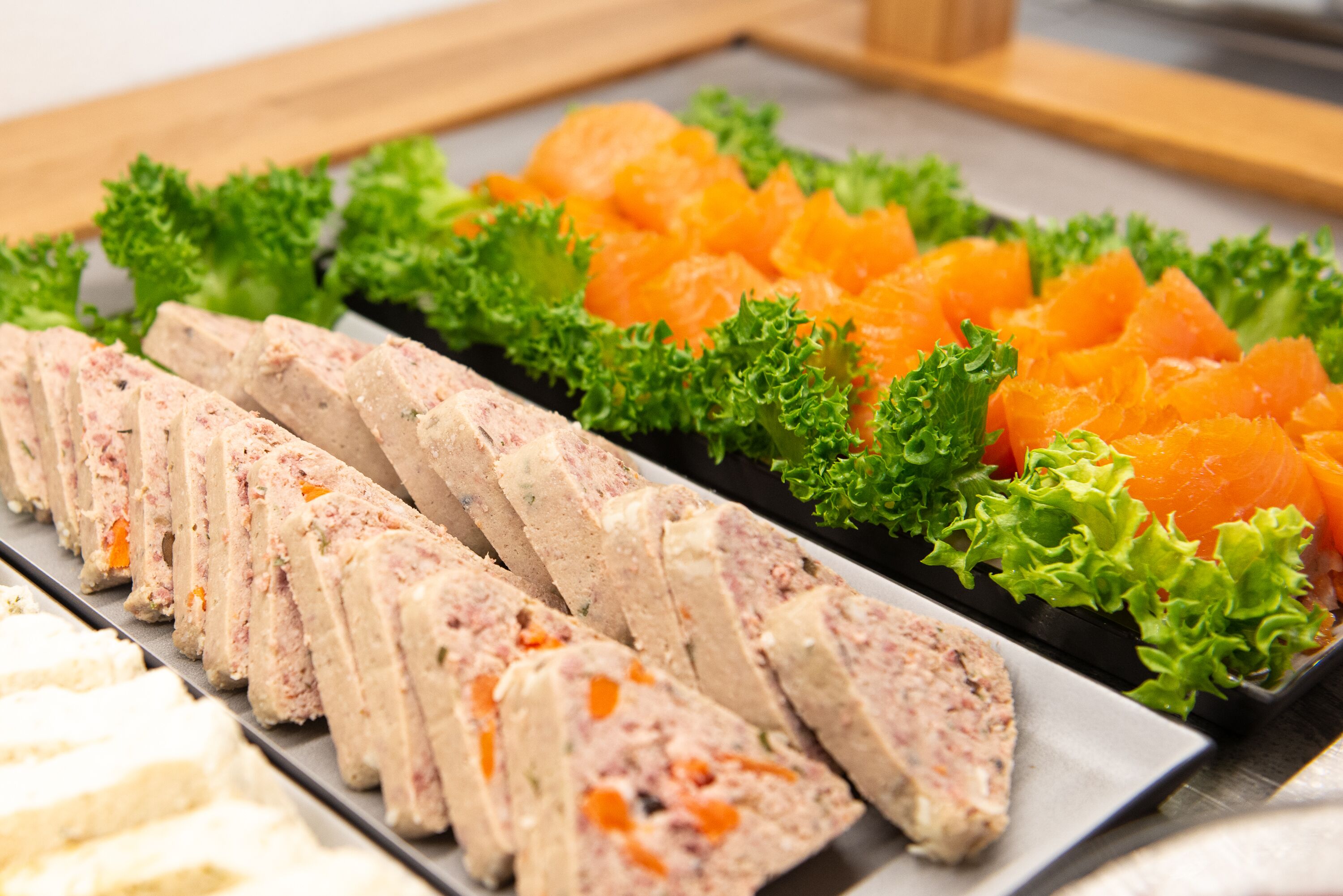 A tray of sliced meatloaf, orange fish, and green lettuce.