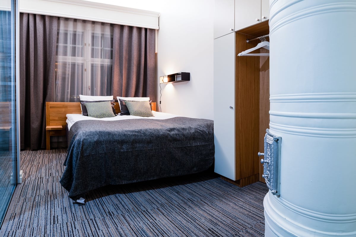 Una habitación de hotel con una cama, una mesita de noche, un armario y un objeto cilíndrico grande.