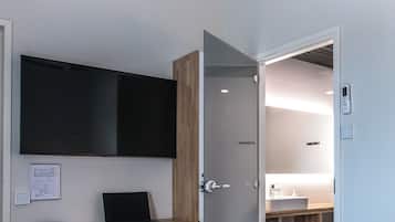 A modern hotel room with a bed, a desk with a laptop, a chair, and a TV mounted on the wall.