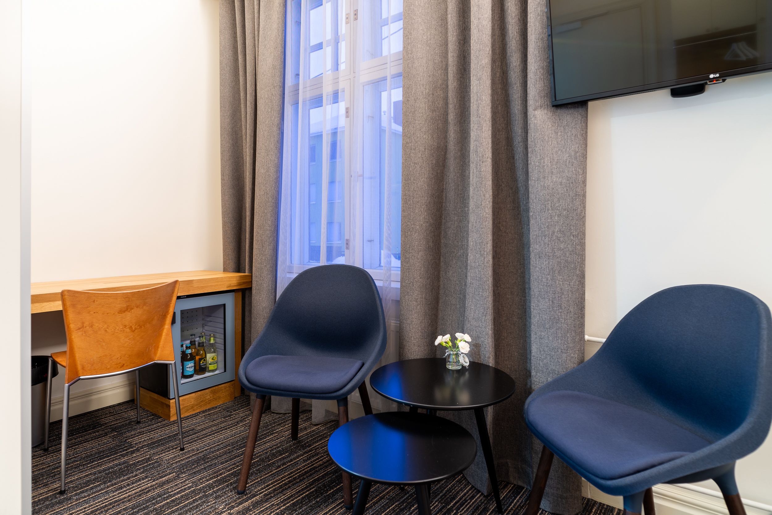 Une chambre d’hôtel avec deux chaises bleues, une petite table ronde, un bureau en bois et un mini-bar.
