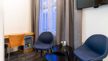 Habitación de hotel con dos sillas azules, una mesita redonda pequeña, un escritorio de madera y un minibar.