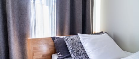 Una cama con cabecera de madera, colchón blanco y tres almohadas con distintos diseños.