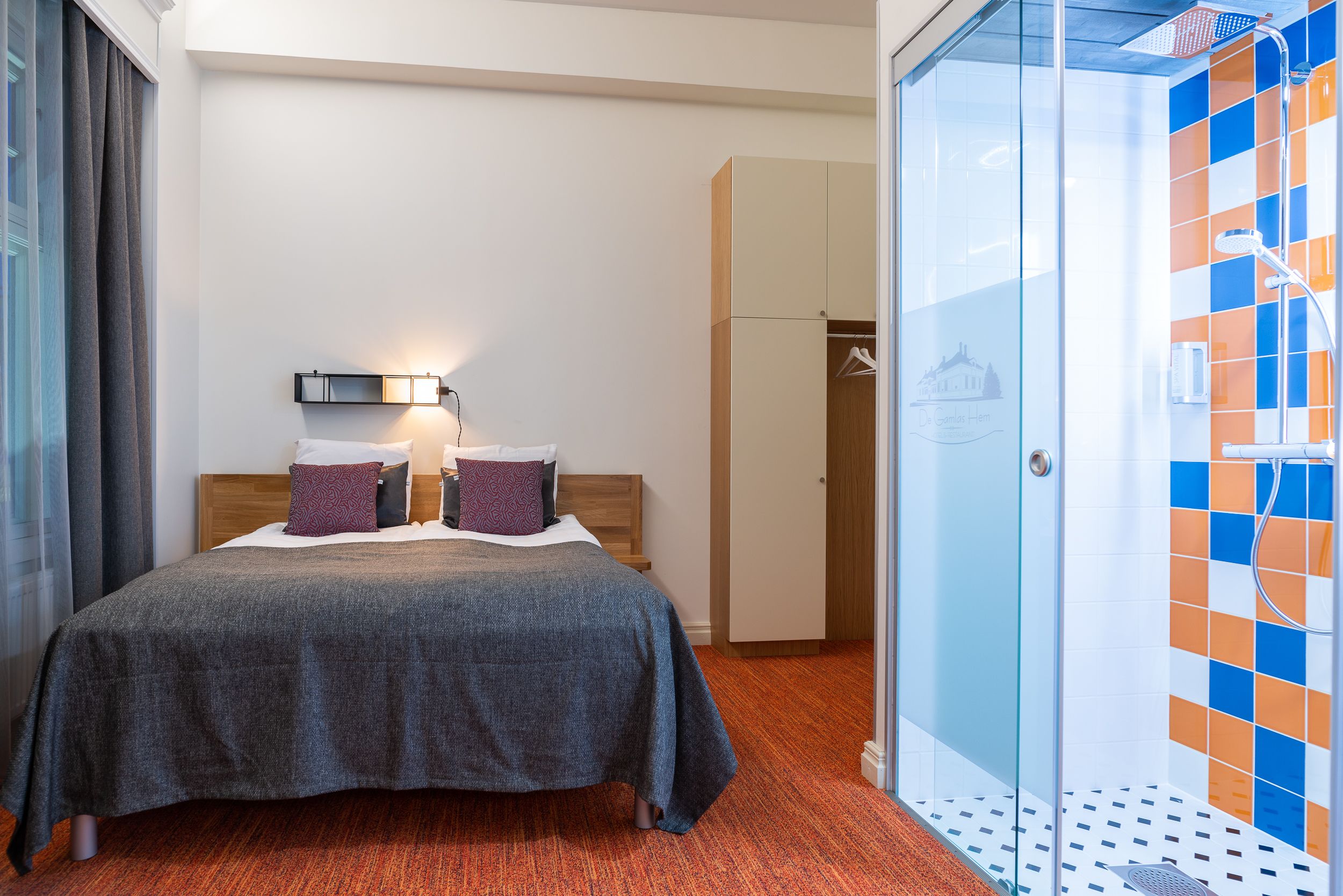Quarto de hotel com cama, armário, área de chuveiro e porta de vidro.