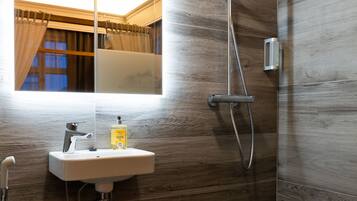 Un baño moderno con pared de madera, un espejo grande, un lavabo con dispensador de jabón y una ducha con cabezal de ducha de mano.