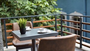A balcony with a table and chairs, a potted plant, and a view of greenery and a building. - Stil Suit (Istanbul)
