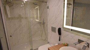 A modern bathroom with a glass-enclosed shower, a white sink with a wooden countertop, and a large mirror. - Stil Suit (Istanbul)