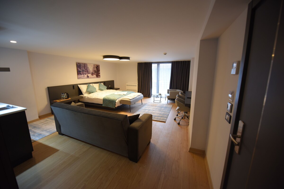 A modern hotel room with a large bed, a sofa, a desk, and a chair.