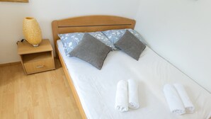Una cama bien hecha con dos almohadas, una mesita de noche con lámpara y una cómoda de madera con cajón.