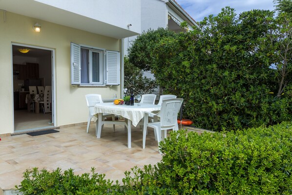 An outdoor patio with a table and chairs, a door leading to a kitchen, and a large bush.
