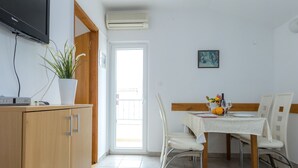 Un comedor con una mesa dispuesta para dos, una planta en maceta y un televisor sobre un mueble.
