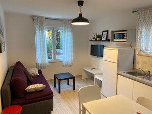 A compact living space with a sofa, a small table, a kitchenette, and a window with curtains.