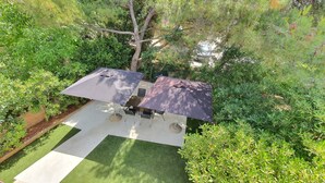 Um terraço ao ar livre com mesa e cadeiras sob dois guarda-sóis, rodeado por vegetação exuberante.
