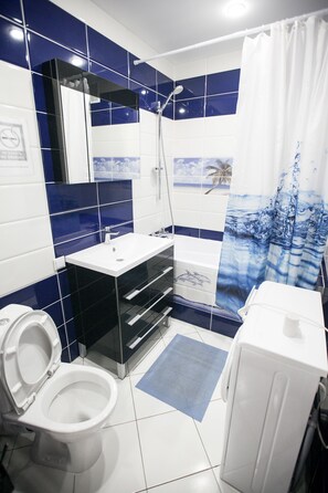 Un baño con inodoro blanco, lavamanos negro, ducha y lavadora blanca.