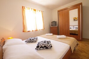 Habitación de hotel con cama, almohadas, televisión, espejo y ventana con cortinas.