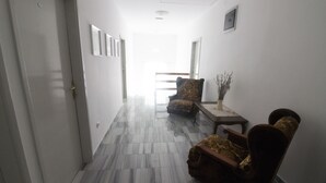 A hallway with a marble floor, two armchairs, a small table with a vase, and a door on the left. - Studios & Rooms Fiesta (Novalja)