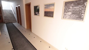 A hallway with a carpet, tiled floor, and a staircase. There are three framed pictures on the wall. - Studios & Rooms Fiesta (Novalja)