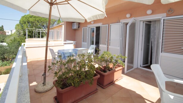 An outdoor patio area with a pool, potted plants, and a white chair. - Studios & Rooms Fiesta (Novalja)