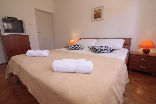 A hotel room with a bed, two bedside lamps, a TV on a cabinet, and a door. - Studios & Rooms Fiesta (Novalja)