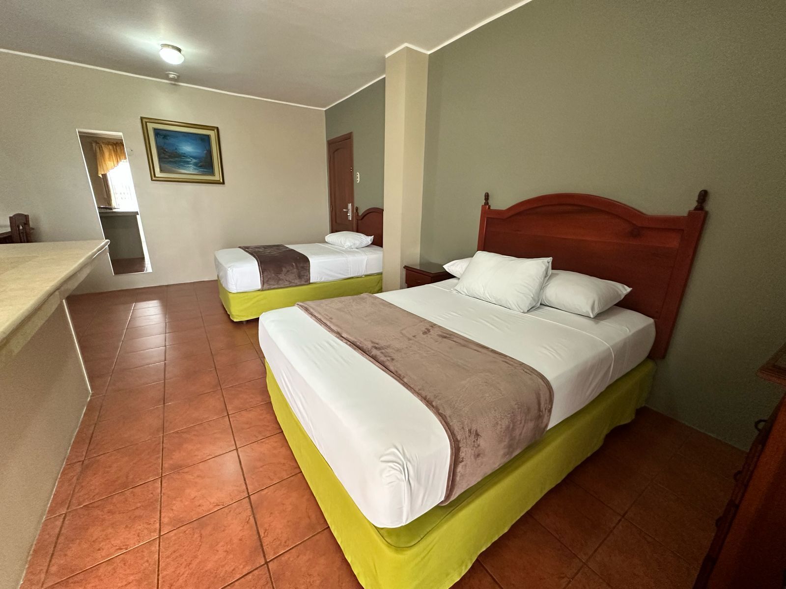 A hotel room with two beds, a wooden headboard, a painting on the wall, and a tiled floor.