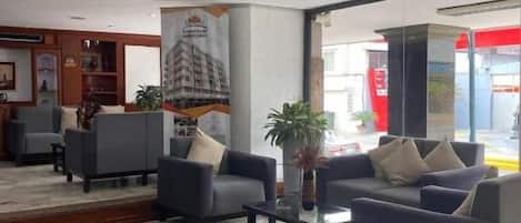 Un vestíbulo de hotel con arreglos de asientos, una mesa de recepción y un ventanal grande.