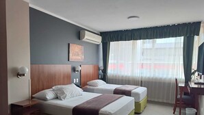 A hotel room with two beds, a desk, and an air conditioning unit. - Grand Hotel Americano (Machala)