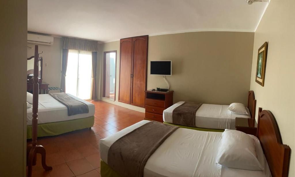 Habitación de hotel con dos camas, televisión, armario y ventana con cortinas.