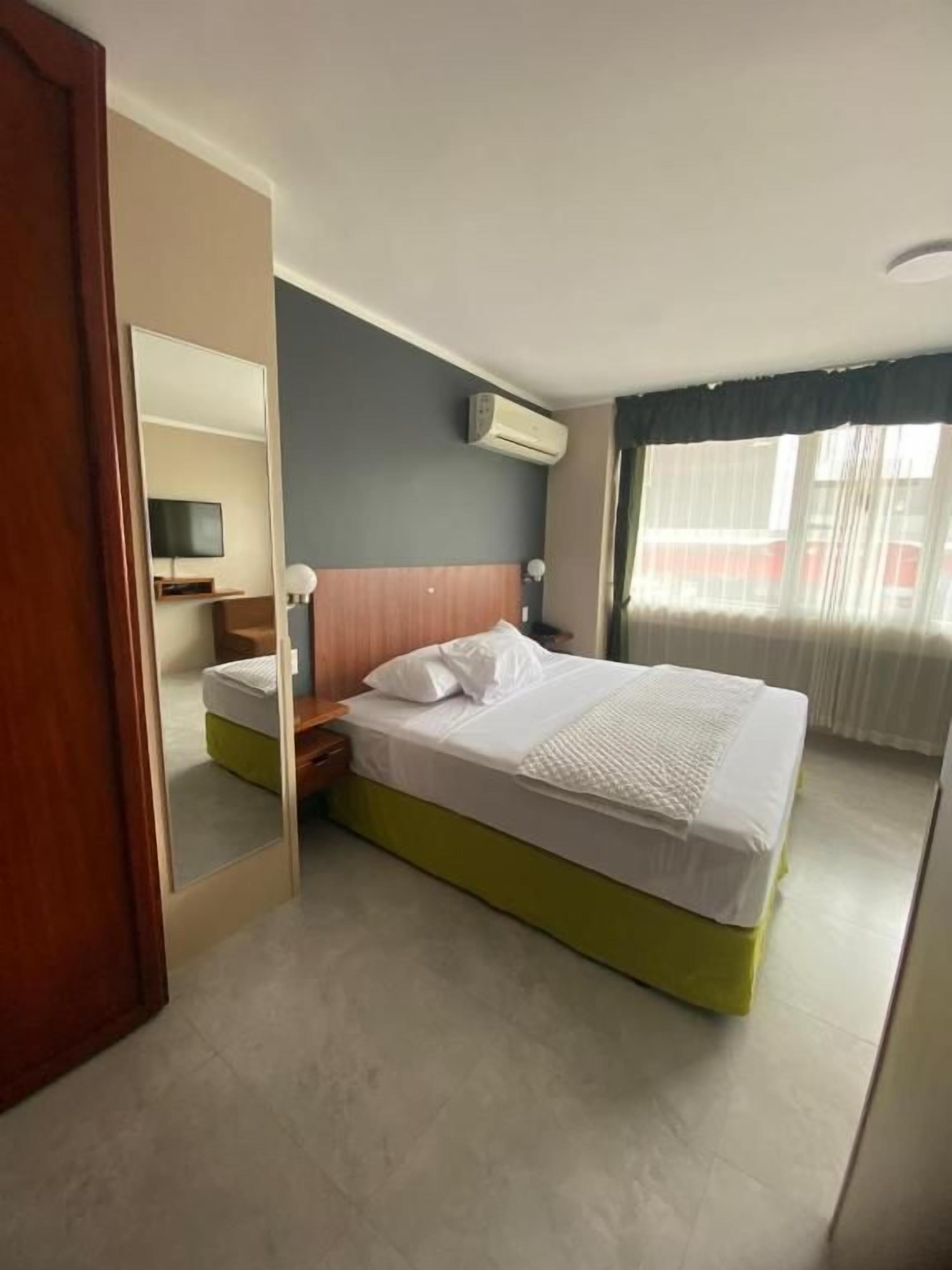 Habitación de hotel con cama, mesita de noche y televisor.