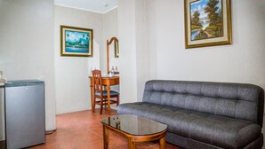 A compact living area with a gray sofa, a wooden dining table with chairs, and a small refrigerator. - Grand Hotel Americano (Machala)
