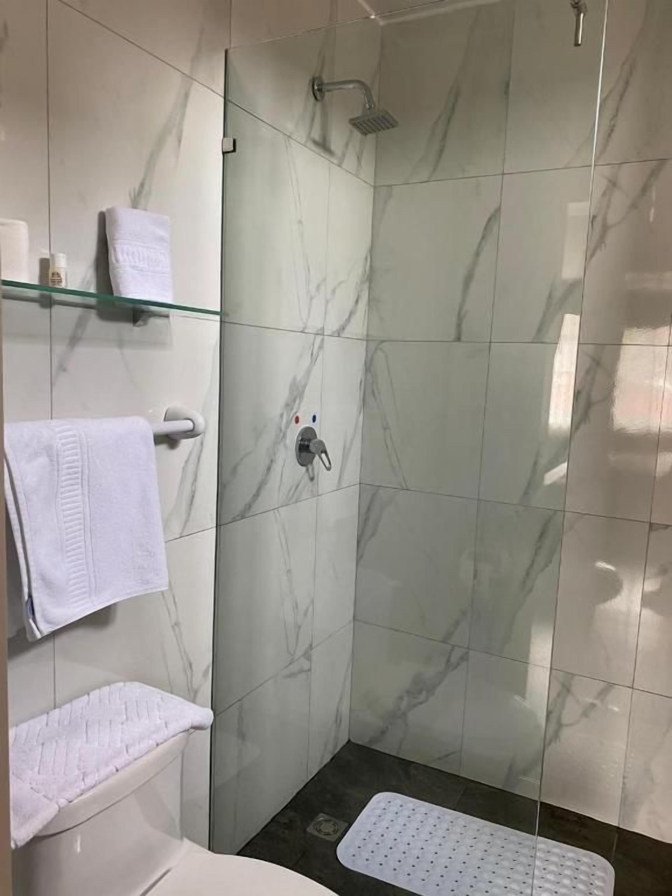 A modern bathroom with a glass shower enclosure, marble tiles, and a white toilet.