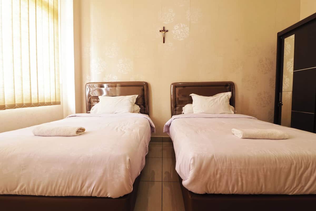 A hotel room with two beds, a cross on the wall, and a door to the right.