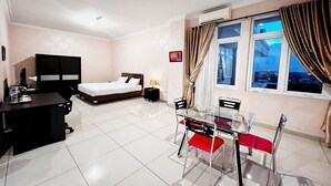 A hotel room with a bed, desk, chair, and a dining table with chairs. - Oase Guesthouse (Medan)