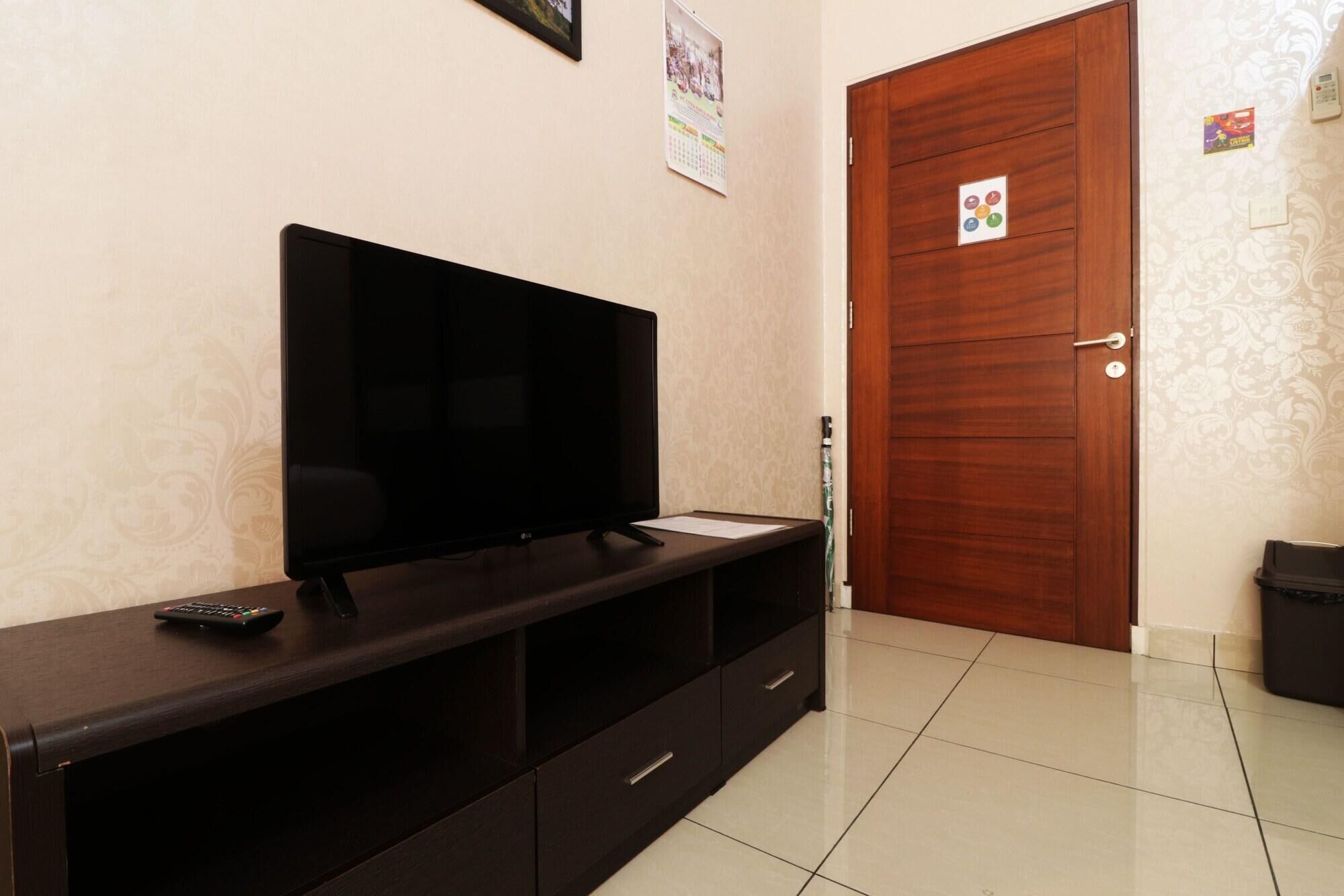 A room with a flat-screen TV on a wooden TV stand, a door with a lock, and a calendar on the wall.