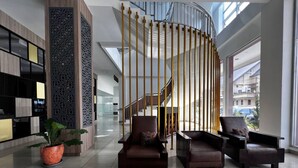 A modern lobby with a curved staircase, leather seating, and a reception area with a decorative screen. - Oase Guesthouse (Medan)
