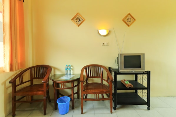 A room with two wooden chairs, a small table with water bottles, a television on a stand, and a blue basket on the floor.
