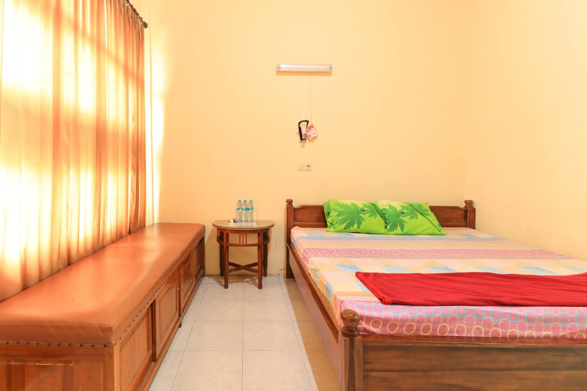 A room with a bed, a bench, a small table with water bottles, and a power outlet on the wall.